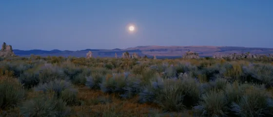 Vollmond über Wüstenlandschaft mit Felsformationen in der Dämmerung