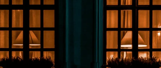 Zwei beleuchtete Fenster mit warmem Lampenlicht in der Dämmerung
