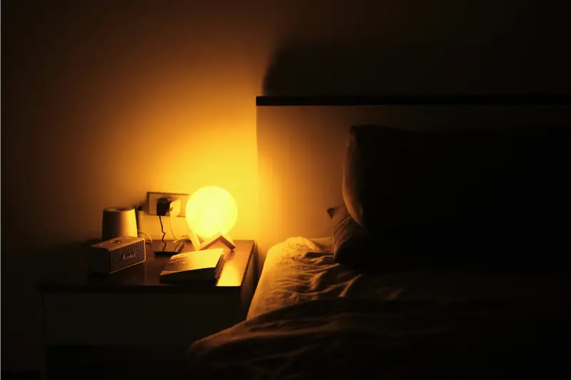 Nachttischlampe leuchtet warm neben Bett im Dunkeln
