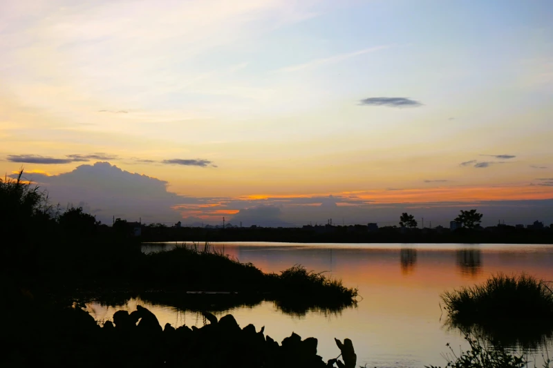 Stille Wasserfläche eines Sees im Abendrot mit Silhouetten am Ufer