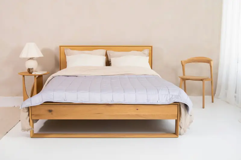 Holzbett mit grauer Steppdecke und Stuhl