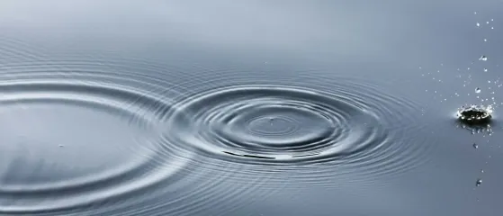Wassertropfen erzeugt Kreise auf ruhiger Wasserfläche