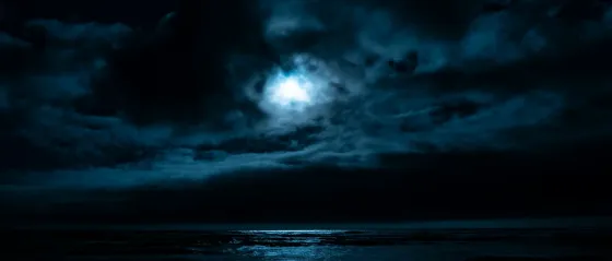 Mond hinter dunklen Wolken über nächtlichem Meer