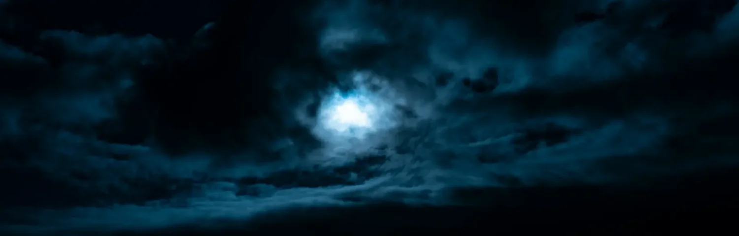 Mond hinter dunklen Wolken über nächtlichem Meer