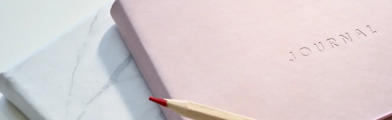 Roter Buntstift auf rosa Notitzbuch