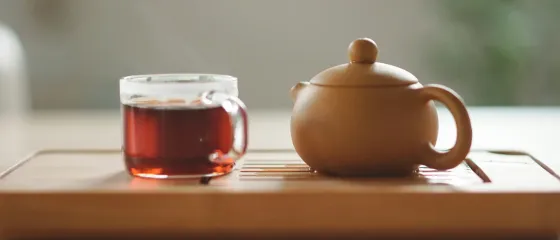 Glastasse mit Tee neben einer braunen Teekanne