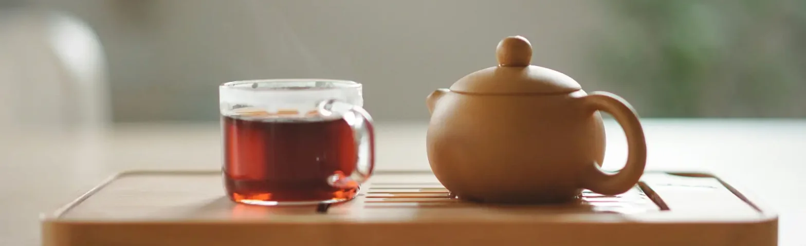 Glastasse mit Tee neben einer braunen Teekanne