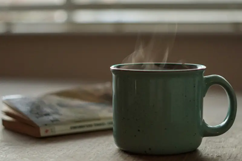 Grüne Tasse mit Dampfendem Tee und einem Buch