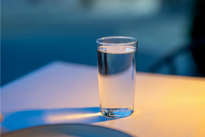 Wasserglas auf Tisch im Abendlicht