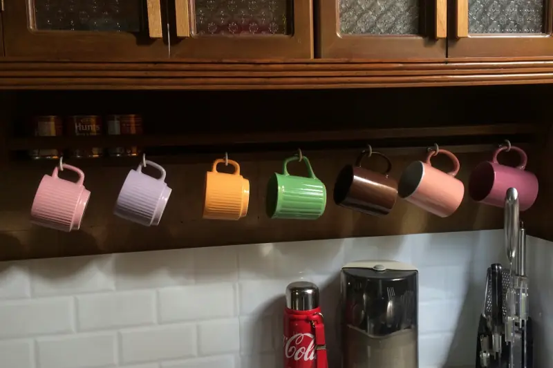 Bunte Tassen hängen in einer Reihe unter einem Holzschrank