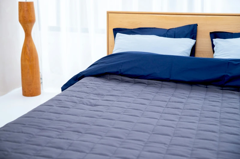 Bett mit gesteppter grauer Decke und dunkelblauer Bettwäsche
