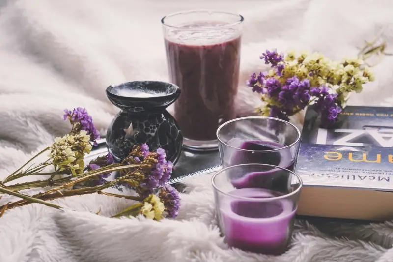 Getränk, Kerzen und getrocknete Blumen auf weißer Decke mit Buch