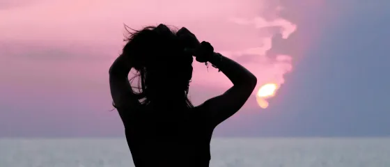 Silhouette einer Frau bei Sonnenuntergang mit Blick aufs Meer