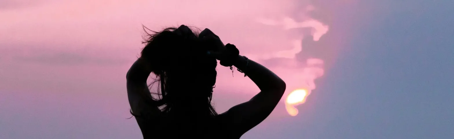 Silhouette einer Frau bei Sonnenuntergang mit Blick aufs Meer