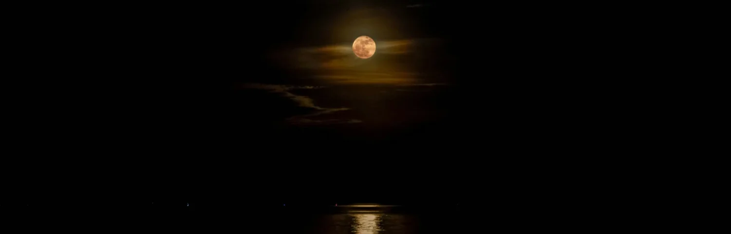 Vollmond über dunklem Meer mit Lichtreflexion auf dem Wasser