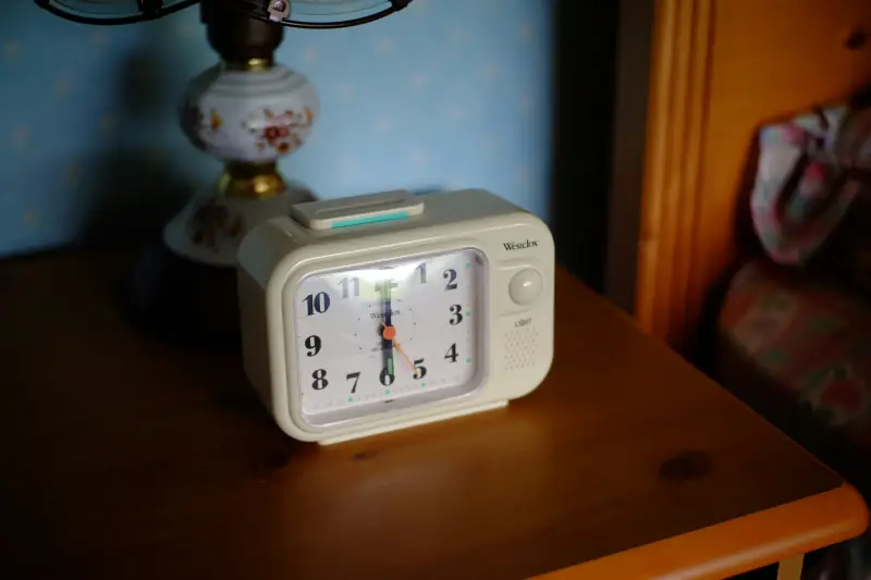 Analoger Wecker auf Nachttisch zeigt 6 Uhr morgens