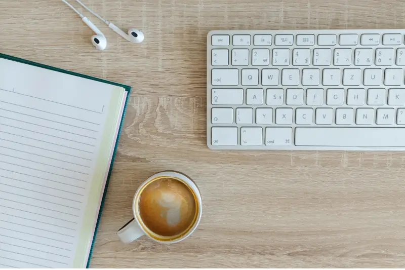 Kaffeetasse neben einer Tastatur und Notizbuch