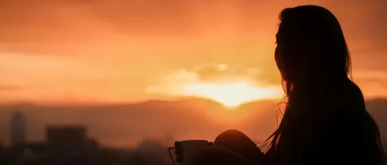 Silhouette einer Frau die den Sonnenuntergang beobachtet