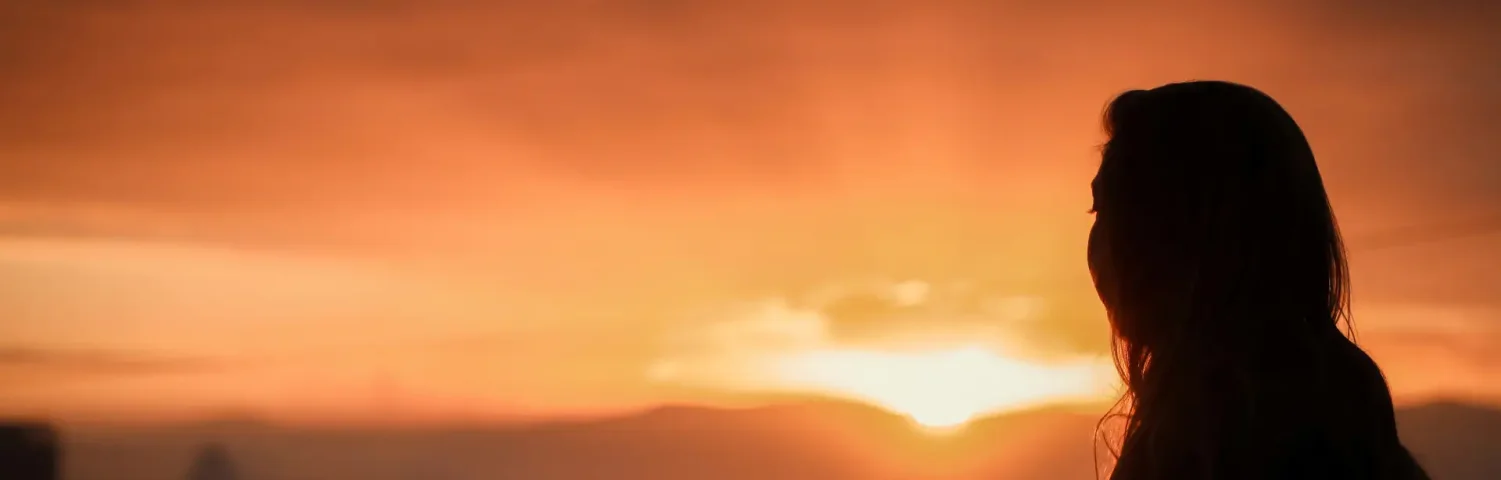 Silhouette einer Frau die den Sonnenuntergang beobachtet